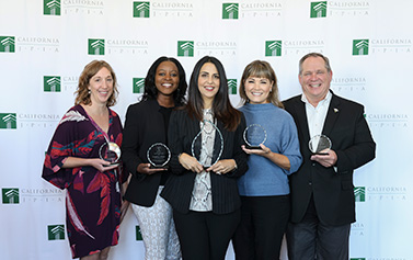 The five 2025 Capstone Award finalists stand together in a row while holding their awards in front of a step-and-repeat banner with the California JPIA's logo.